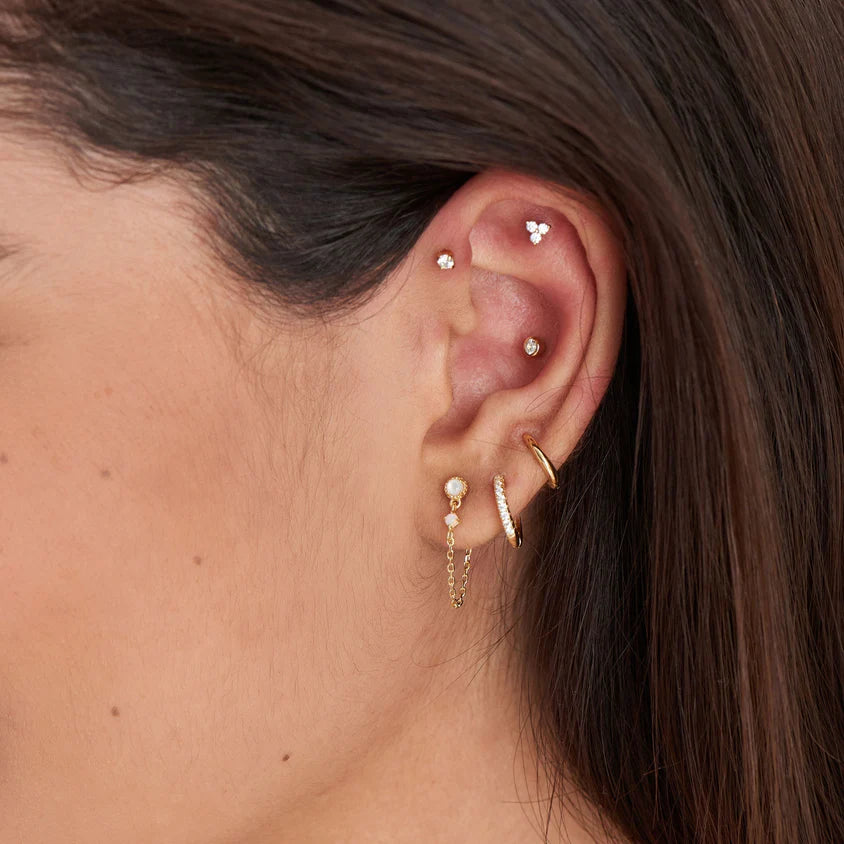 Close-up of an ear with gold earrings and pearl studs.