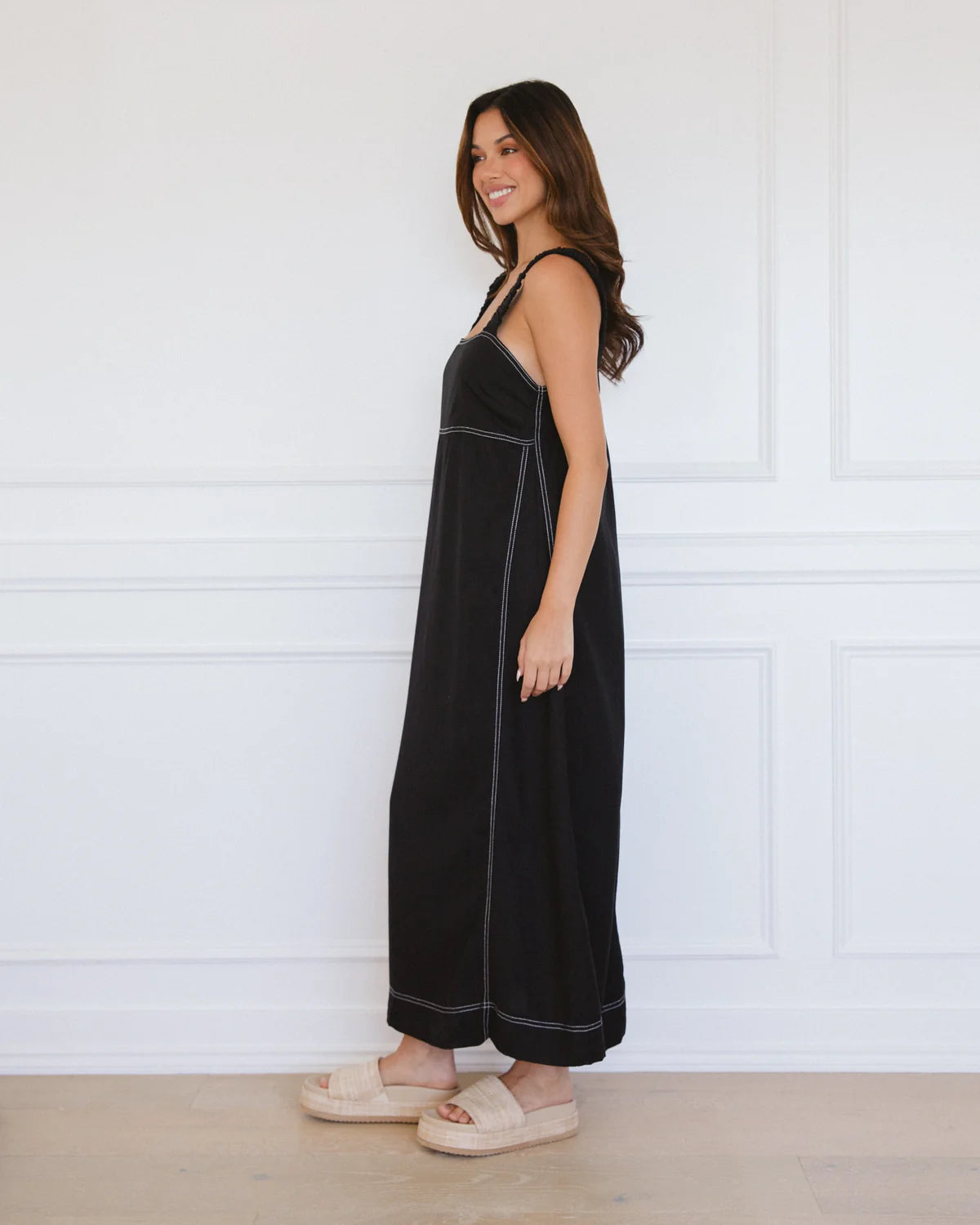 Woman wearing a black dress with white trim against a white wall.