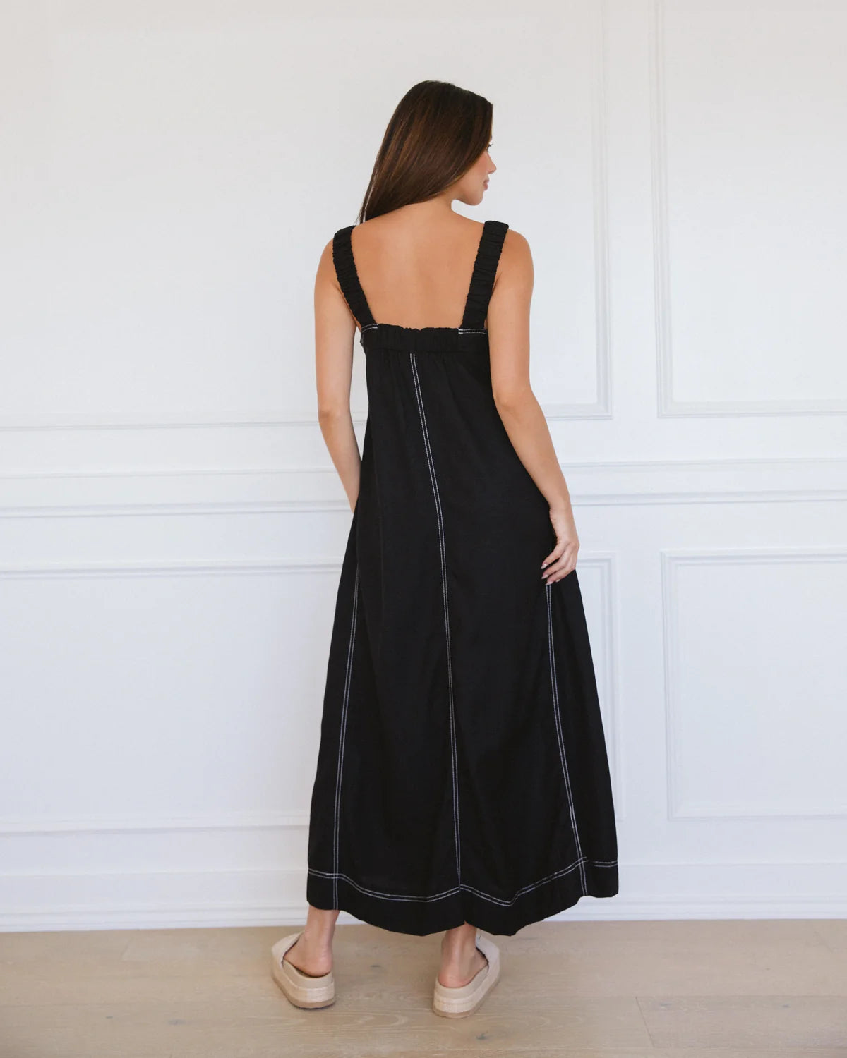 Woman wearing a black dress with white trim against a white wall.